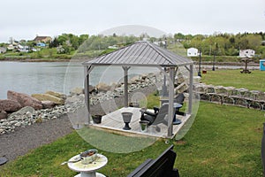 A gazebo with chairs and a small table next to old-fashioned lobster traps and a walking path on the shoreline of Mulgrave. photo