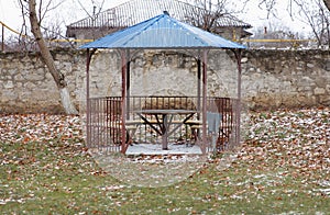 A gazebo located outdoor with a table and benches inside, made of metal with a blue roof. A place of relaxation