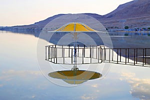 The gazebo for protection from the sun reflected in Dead Sea water at sunset