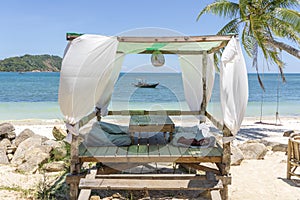 Gazebo for relaxing with white curtains on tropical sand beach near blue sea water on island Koh Phangan, Thailand