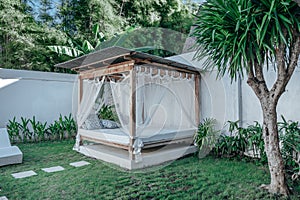 Gazebo with a wooden bed under a mosquito grid on a outside
