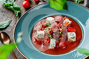 Gazpacho tomato cream soup with cucumbers, bell pepper, greens and feta cheese in plate on wooden background. Healthy vegan food,