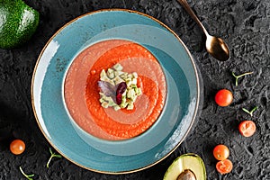 Gazpacho tomato cream soup in plate with avocado and greens over dark background.