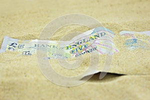 GBP Five Pound note covered in sand