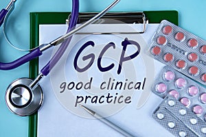 GCP - acronym on a white piece of paper on a blue background. A stethoscope and pills lie side by side