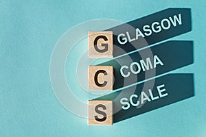 GCS Glasgow Coma Scale text, written on wooden blocks with shadows on blue background