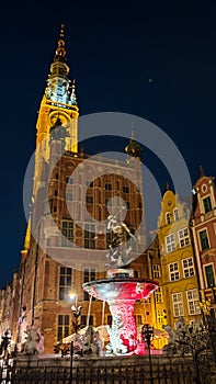 Gdansk - The Neptune's Fountain in Old Town of Gdansk, Poland at night. The fountain is lit with red and white lights.