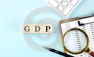 GDP word on wooden cubes on blue background with chart and keyboard