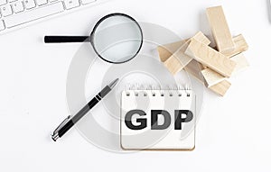 GDP word written on notebook with block magnifier and pen , business concept