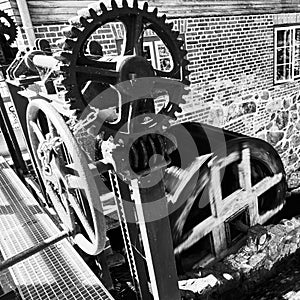 Gear and control unit of a hisoric water mill in front of the turning mill wheel with motion blur, black and white, hard contrast