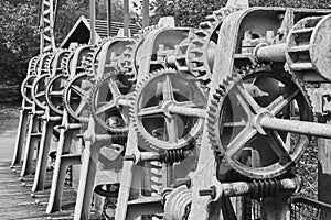 Gear wheels, toothed belts, chains, shafts and racks at a weir on the river Aller, Germany, black and white