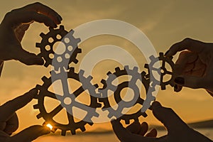 Gears in the hands of a team of people against the sunset