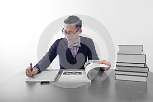 Geek chic: man writing on notepad, with open book and stack of books on desk