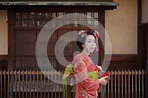 Geisha in a kimono walking in front of the gate of a traditional