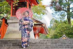 Geishas girl wearing Japanese kimono among red wooden Tori Gate at Fushimi Inari Shrine in Kyoto, Kimono is a Japanese traditional