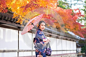 Geishas girl wearing Japanese kimono among red wooden Tori Gate at Fushimi Inari Shrine in Kyoto, Kimono is a Japanese traditional