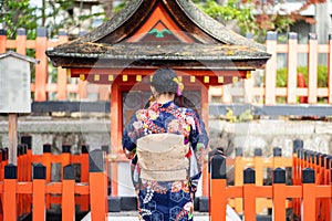 Geishas girl wearing Japanese kimono among red wooden Tori Gate at Fushimi Inari Shrine in Kyoto, Kimono is a Japanese traditional