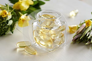 Gel capsules of evening primrose oil in a bottle with fresh flowers