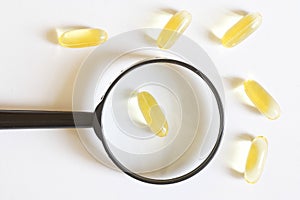 Gel capsules with yellow medicine and a magnifier on a white background. Research and testing of drug efficacy. Search for the