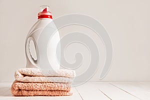 Gel for laundry washing in a white unnamed plastic bottle, standing on a fresh colored towels. Composition on white