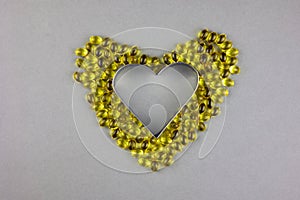 Gel yellow capsules with vitamin D3 on a gray background, laid out in the shape of a heart