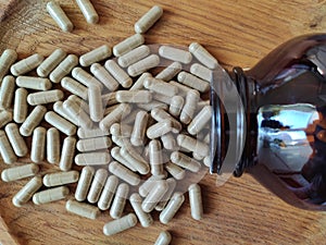 gelatin capsules with vitamins are scattered on a wooden plate and the neck of a brown glass bottle