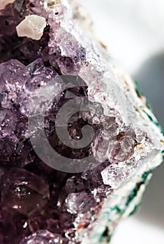 Gemstone Amethyst closeup as a part of cluster geode filled with rock Quartz crystals.