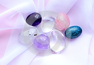 Gemstone minerals on a pink background. Round tumbling minerals of amethyst, rose quartz, rock crystal and apatite on white