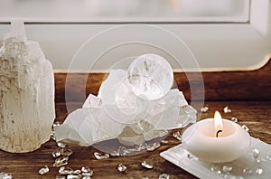 Gemstone sphere or crystal ball on quartz geode on wood tray, candle burning.