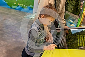 Gen Alpha boy interacts with an interactive screen, exploring and seeking information with an adult photo