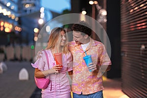 Gen Z couple in pink outfits leaving the cinema with drinks in hand.