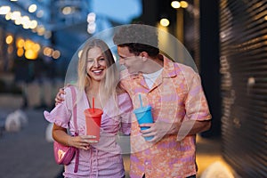 Gen Z couple in pink outfits leaving the cinema with drinks in hand. The young zoomers watched movie addressing topic of
