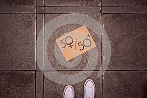 Gender equality concept as woman legs and paper sheet with male and female symbol over crowded city street background. Woman