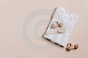 Gender neutral baby garment. Set of organic cotton bodysuit, romper, wooden toys on beige background. Flat lay, top view