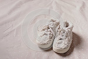 Gender neutral baby teddy shoes and accessories over beige background. Top view, copy space