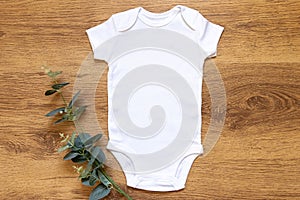 Gender neutral blank white babygrow on a wam wooden background