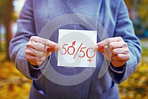 Gender parity concept. closeup caucasian woman shows paper with written text fifty with zeros as male and female gender symbols.