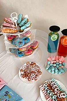 Gender party, blue and pink balloons on the background, close-up of a festive table with cake, lemonades, donuts and pretzels