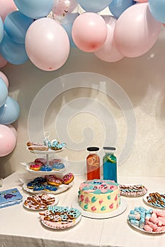 Gender party, blue and pink balloons on the background, close-up of a festive table with cake, lemonades, donuts and pretzels