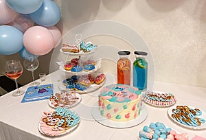 Gender party, blue and pink balloons on the background, close-up of a festive table with cake, lemonades, donuts and pretzels.