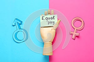 Gender pay gap. Wooden mannequin hand with paper note, male and female symbols on color background, flat lay