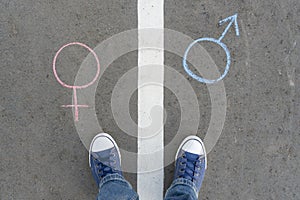 Gender symbol of a man and a woman drawn in chalk on the asphalt. A man`s feet stand on the road markings between the gender