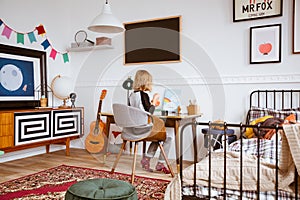 Genderless bedroom with kid painting at the retro desk in tenement house