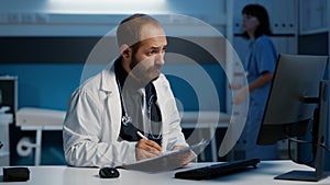 General practitioner checking medical report on computer comparing with expertise written on paper