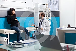 General practitioner consulting pregnant woman in cabinet