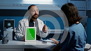 General practitioner explaining patient disease symptoms to nurse pointing at tablet computer with green screen