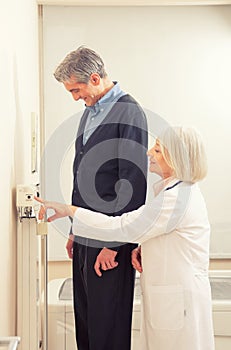 General practitioner measuring male patient's height in hospital