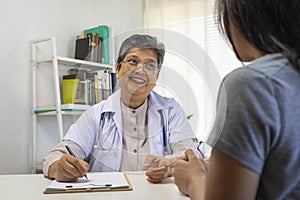 General practitioner taking notes when talking to female patient in hospital.