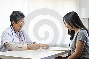 General practitioner taking notes when talking to female patient in hospital.