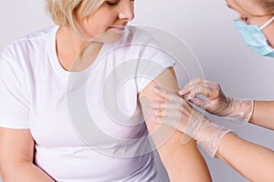 General practitioner vaccinating female patient in clinic. Doctor giving injection to senior woman at hospital. Nurse